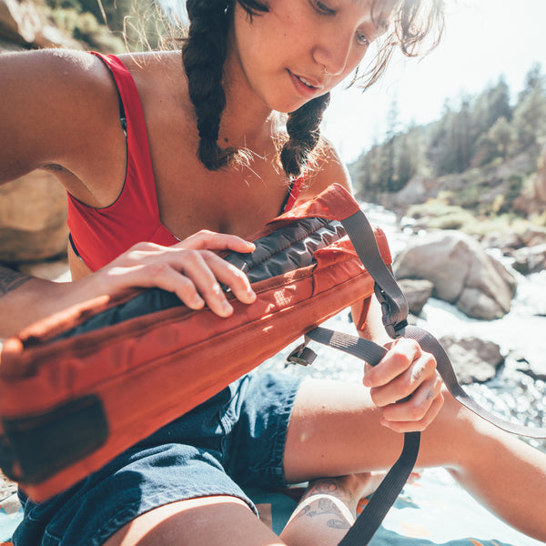 Woman sitting in a forest rolling up her crazy creek chair in copper