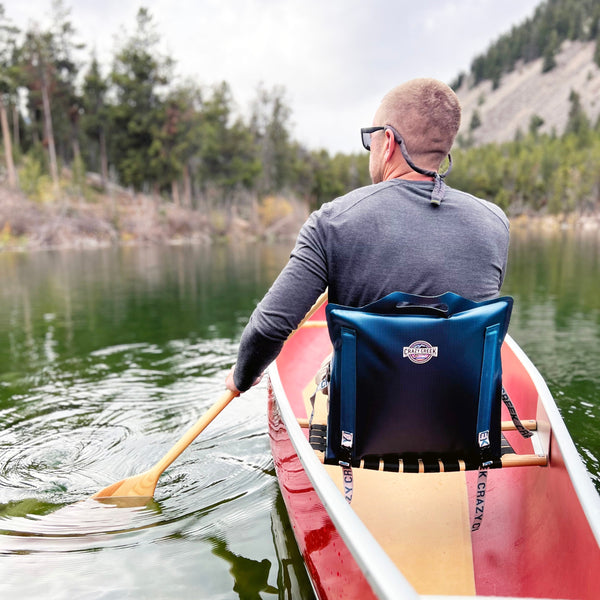 Man paddling a canoe on a beautiful lake while he is sitting in a comfortable canoe chair