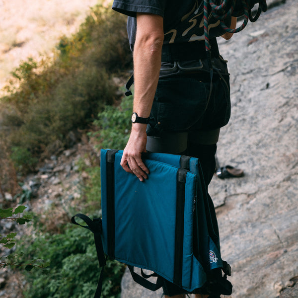 Rock climber holding folded casual crazy creek chairs in the mountains