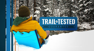 Trail Tested Guarantee - Person sitting in deep snow in an inflatable and insulating chair in front of a cold river