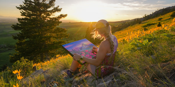 Rachel Pohl sitting on a hillside at sunset, painting a landscape.