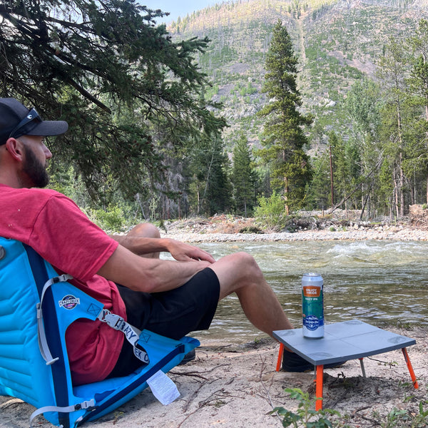 Man sitting next to a river in the mountains with the table holding a beer