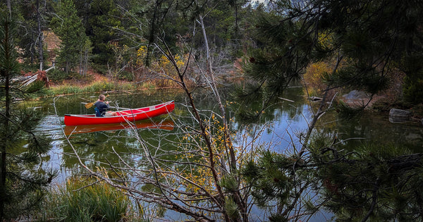 Wide shot of a man paddling down a river in a right red canoes sitting in a comfortable crazy creek chair
