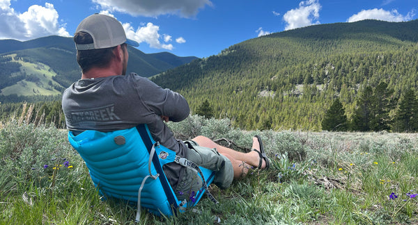 A man reclining comfortably in a green hillside in his inflatable blue crazy creek chair