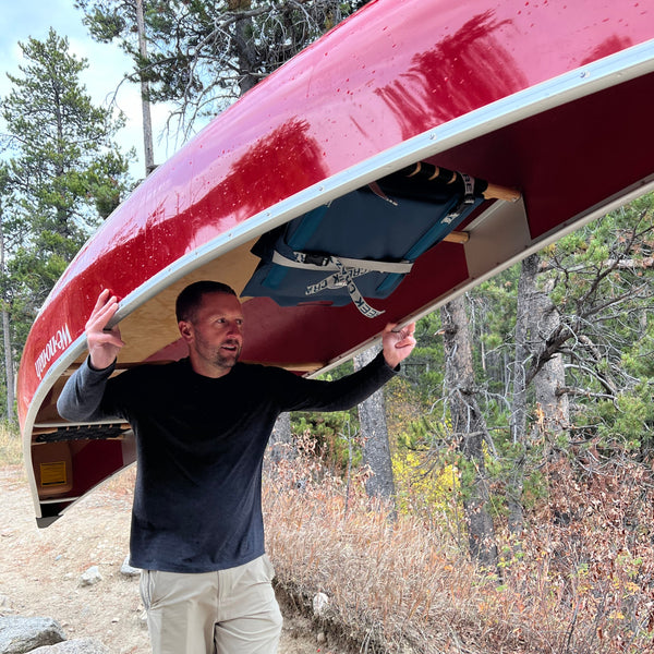 Man portaging is canoe with paddle chairs in storage mode attached to the seats