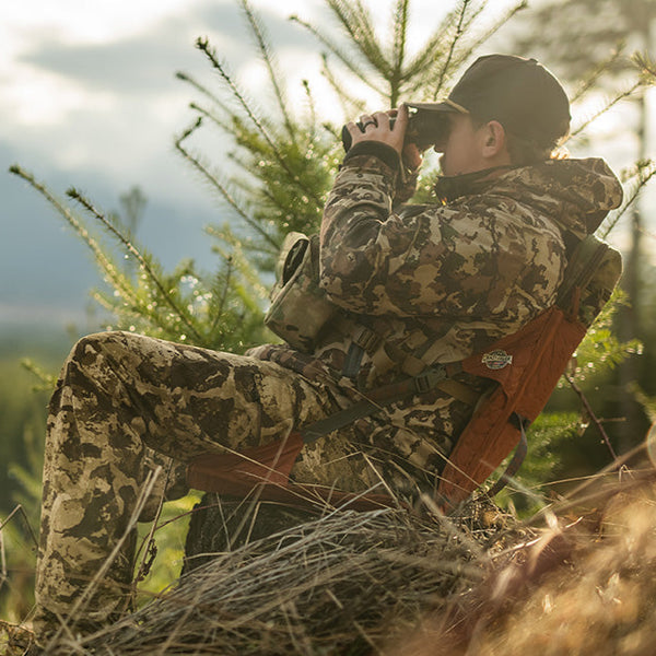 Man dressed in camo looking through binoculars while sitting in a copper hex chair