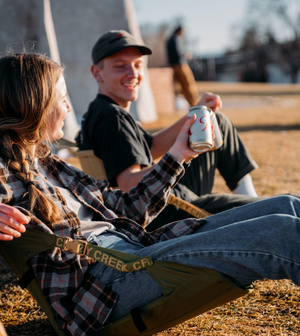 Two people sitting in crazy creek chairs sharing a drink