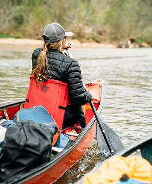 Woman paddling down a river in a canoe while sitting in a red crazy creek chair.