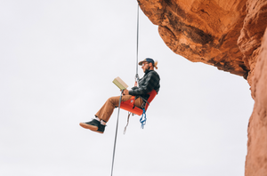 Man rock climbing while sitting in a red chair and reading a book