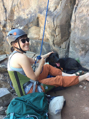 Person with dog at the base of a rock climbing crag sitting in a crazy creek chair