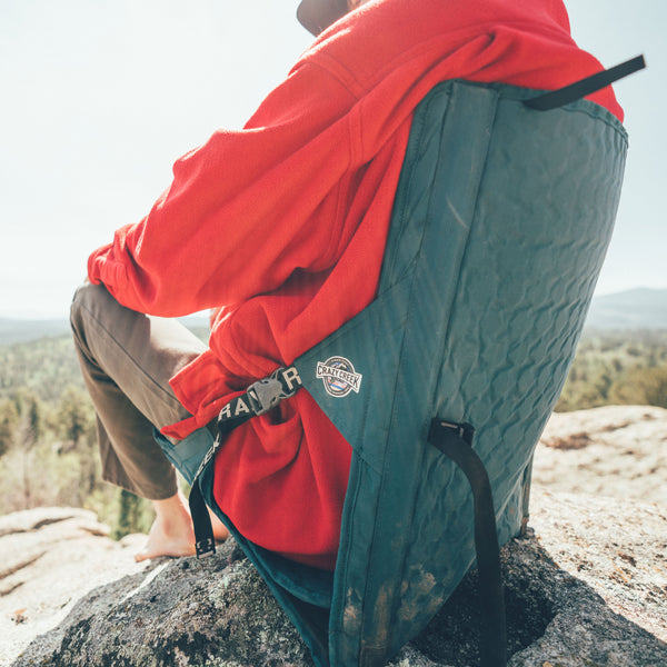 Person sitting on a rock wearing a red jacket sitting in a green crazy creek camping chair