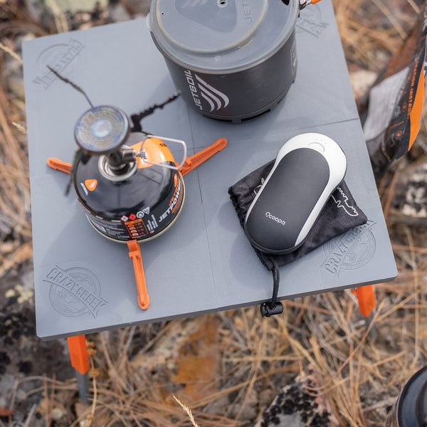 Closeup of the top of the table while camping holding a stove pot and small electronic device