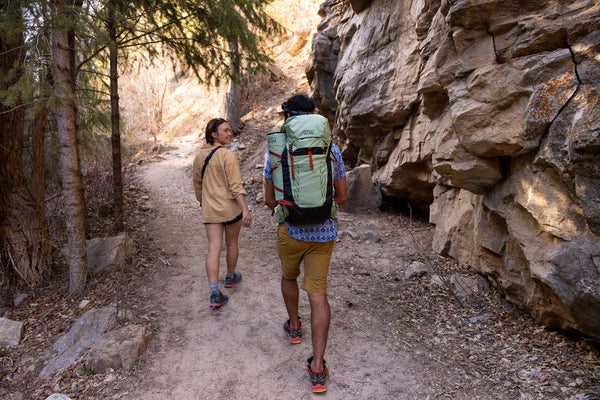 Woman and Man going on a hike in the forest with their Osprey x Crazy Creek Talon backpack and Chair