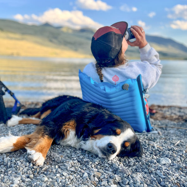 Woman and her dog lounging on the edge of a lake while sitting in a comfy inflatable camping chair