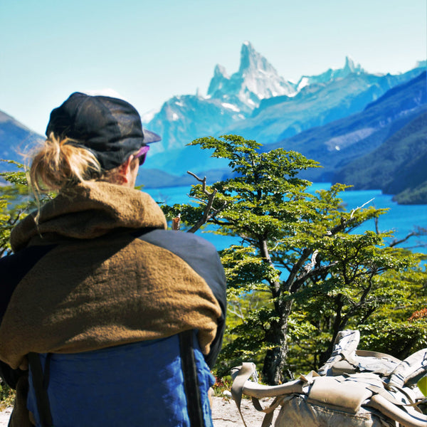 A person looking out over a blue lake and pointy mountains