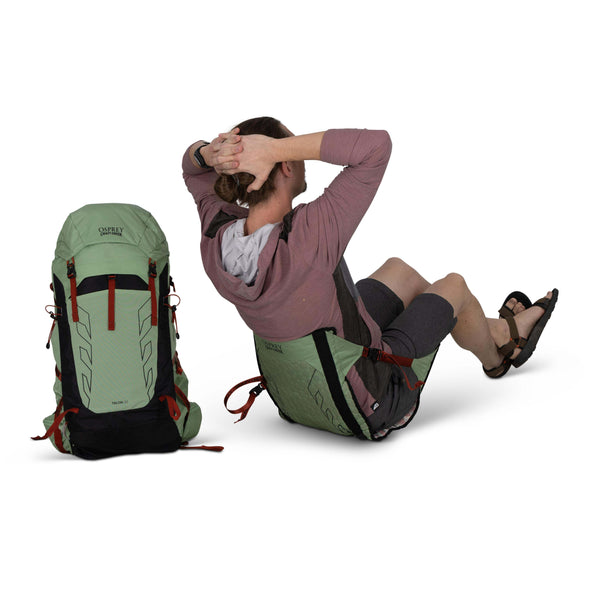 Backpacking man sitting - facing away  in the Osprey and Crazy Creek Collab Hex chairon white - with backpack sitting next to him